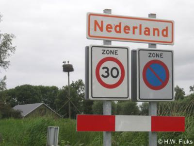 Nederland, plaatsnaambord (juli 2010) met op de achtergrond het op dat moment bewoonde ooievaarsnest. Volgens ons het enige oranje op witte plaatsnaambord van ons land.