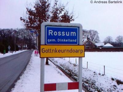 Rossum, met het officiële plaatsnaambord en het carnavalsbord eronder (jan. 2010). De carnavalsvereniging schrijft het zelf op haar site overigens met één t.